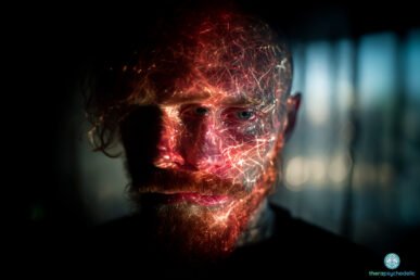 Portrait d’un homme barbu plongé dans l’obscurité, le visage illuminé par des motifs lumineux évoquant des réseaux neuronaux, symbolisant un bouleversement de la perception.