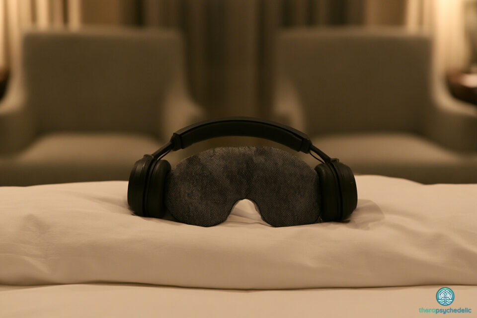 Casque audio et masque oculaire posés sur un lit, entourés de deux fauteuils vides, symbole de la musique de séance après un traitement à la psilocybine.