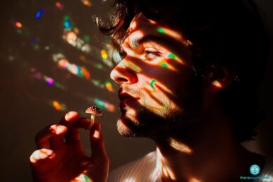 Homme de profil tenant un champignon psychédélique sous des jeux de lumière multicolores illustrant le recours aux thérapies assistées.